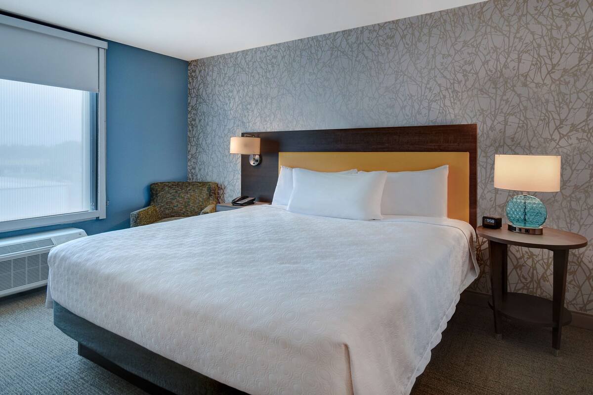 A hotel room with a large bed, two bedside lamps, a small table with a globe, and a chair.