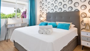 A neatly made bed with a grey headboard, a window with blue curtains, and a wall with a circular pattern.