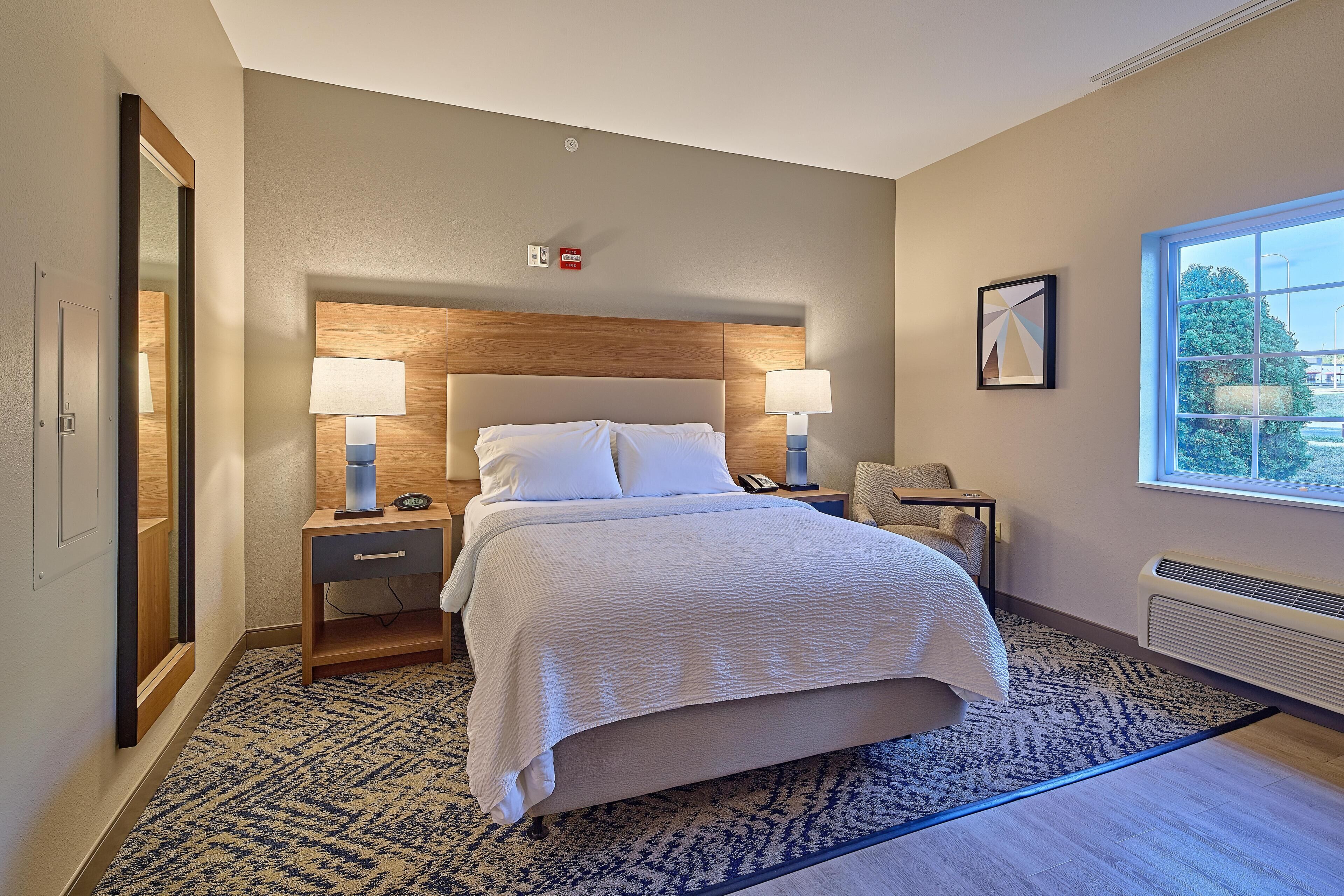 Une chambre d’hôtel comprenant un lit, deux tables de chevet avec des lampes, une chaise, une fenêtre donnant sur un paysage agréable et un tableau accroché au mur.