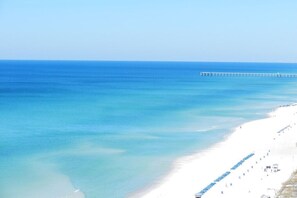 A beach with a long pier extending into the ocean, a sandy shoreline, and a clear sky.
