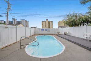 A swimming pool with a metal ladder, surrounded by a white fence, with buildings in the background. - Nittany South, Luxury Rental, Block from Beach, Ocean View Balcony, Game Room (North Myrtle Beach)
