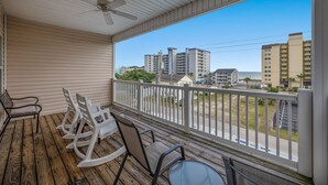 Une terrasse en bois avec des fauteuils à bascule et une table, d’où l’on a une vue sur un quartier résidentiel avec ses immeubles et un ciel dégagé.