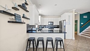 Una cocina moderna con armarios blancos, una isla central con taburetes y estrellas de mar decorativas en estantes.