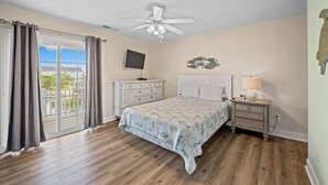 Un dormitorio con una cama grande, ventilador de techo, televisor, cómoda y mesita de noche.