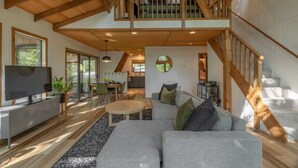 Ein geräumiger Wohnbereich mit hohen Decken, Holzbalken, einer Treppe und Blick ins Freie.