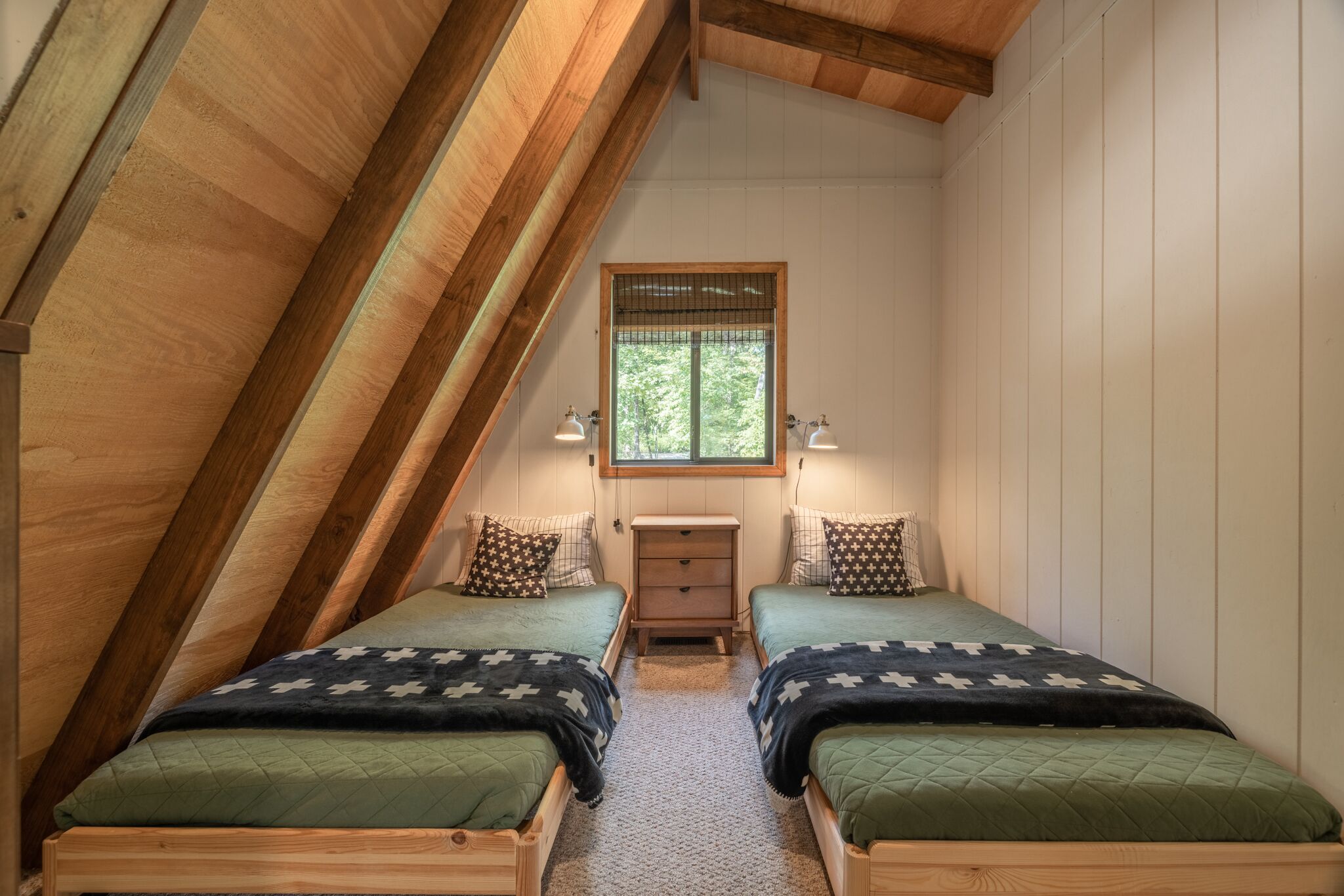 A small, cozy attic bedroom with two single beds, a nightstand, and a window.