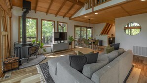 Ein geräumiger Wohnbereich mit einer großen, grauen Couch, einer Holzbalkendecke und einer modernen Küche im Hintergrund.