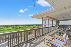 Una terraza techada con mobiliario exterior, barandilla y vista a la playa.