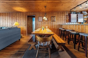 Interior de madera con una mesa de comedor, sillas, un sofá y una cocina con ollas colgantes.