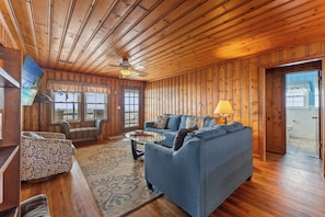 A wooden-paneled room with a sofa, a coffee table, and a ceiling fan. - Covington Cottage, Oceanfront Cherry Grove Home (North Myrtle Beach)