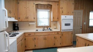 A compact kitchen with wooden cabinets, a white stove, a sink, and a refrigerator. - Nautical Winds, Beach House in Cherry Grove, Just Steps From the Beach (North Myrtle Beach)
