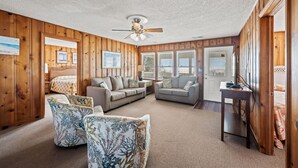 Une pièce chaleureuse avec des lambris en bois, un ventilateur de plafond et un coin salon comprenant deux canapés et deux fauteuils à motifs.