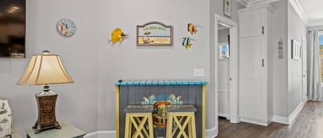A hallway with a wooden floor, a small table with a lamp, and wall decorations including a clock and a sign.