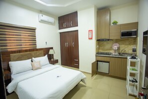A hotel room with a bed, a small kitchenette, a wooden wardrobe, and a wall-mounted air conditioner. - Prestige Resident Apartments and Homes (Abuja)