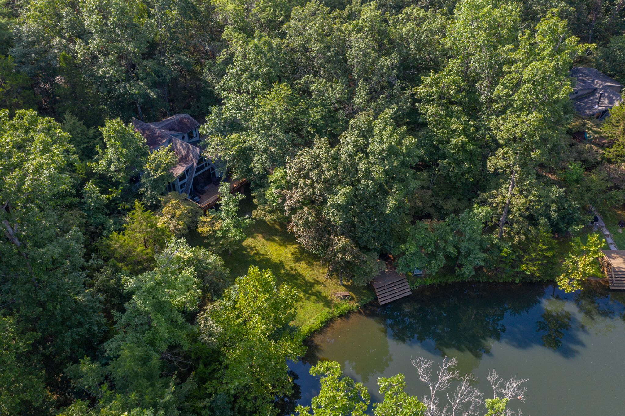 Une vue aérienne d’une zone boisée, avec une petite cabane et une jetée qui s’avance dans un plan d’eau.