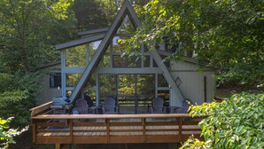 Une terrasse en bois avec des fauteuils Adirondack et un barbecue, donnant sur une zone boisée.