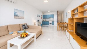 A modern living room with a sofa, coffee table, and TV, a kitchen with blue cabinets, and a dining area. - Jardines Apartment 1 (Puerto del Carmen)