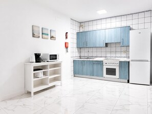 Una cucina moderna con mobili bianchi, un frigorifero bianco, un forno a microonde, una macchina da caffè e un lavello. Sulla parete, tre quadri incorniciati.