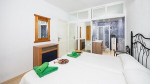 Un dormitorio con cama, cómoda de madera, espejo, armario y baño con ducha, además de una ventana.