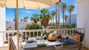 Un balcón con mesa lista para comer, con vista a palmeras y al mar.