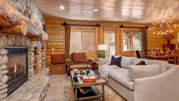 A log cabin interior with a stone fireplace, wooden walls, a sofa, a coffee table, and a lamp. - Abode at Black Bear #151, remodeled, hot tub, steps to Deer Valley (Park City)