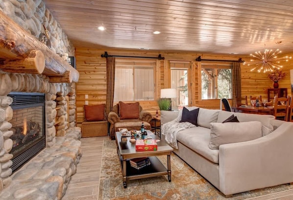 A log cabin interior with a stone fireplace, wooden walls, a sofa, a coffee table, and a lamp.