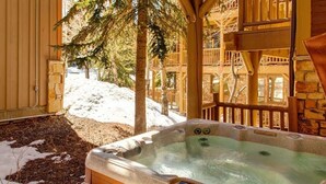 A hot tub with a stone exterior, surrounded by a wooden deck and a stone wall, with snow on the ground. - Abode at Black Bear #151, remodeled, hot tub, steps to Deer Valley (Park City)