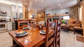 A wooden interior with a dining table set for four, a stone fireplace, and modern kitchen appliances. - Abode at Black Bear #151, remodeled, hot tub, steps to Deer Valley (Park City)