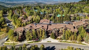 A resort with multiple buildings surrounded by trees, a central road, and a view of distant mountains. - Abode at Black Bear #151, remodeled, hot tub, steps to Deer Valley (Park City)