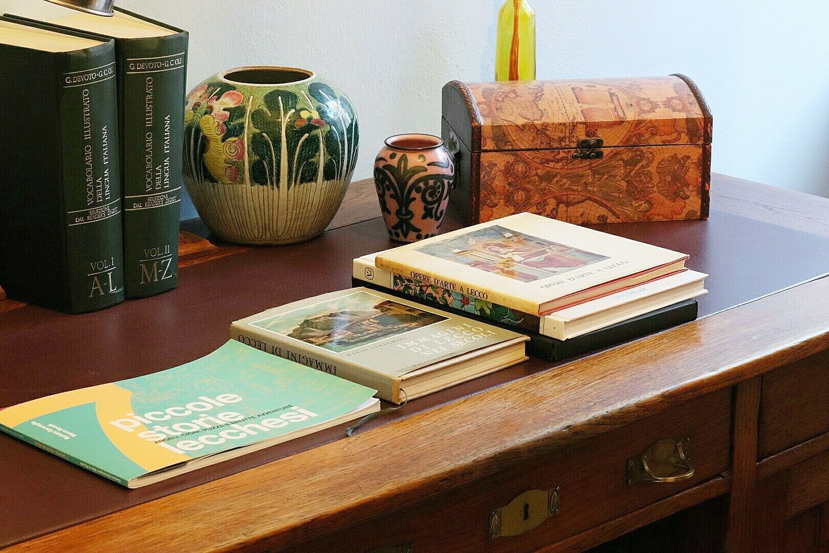 Un escritorio de madera con libros, un florero de cerámica y un cofre de madera.