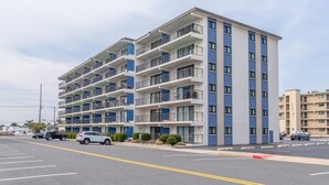 Un hôtel à plusieurs étages, doté de balcons à chaque niveau, d’un parking à l’avant et surplombant un ciel dégagé.