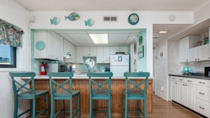 Une cuisine avec des meubles blancs, un plan de travail en bois et des chaises de couleur turquoise.