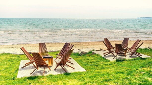 A beachside seating area with lounge chairs and a table, overlooking the sea. - Cottage 18: Lower-Level Beachfront Unit in 4-Plex (Wainfleet)