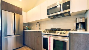 A modern kitchen with stainless steel appliances, wooden cabinets, and a tiled backsplash. - Cottage 18: Lower-Level Beachfront Unit in 4-Plex (Wainfleet)