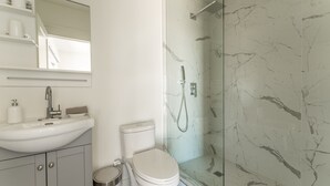 A bathroom with a white sink, toilet, and glass-enclosed shower. - Cottage 18: Lower-Level Beachfront Unit in 4-Plex (Wainfleet)