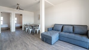 A modern living room with a grey sectional sofa, a dining area with a table and chairs, and a ceiling fan. - Cottage 18: Lower-Level Beachfront Unit in 4-Plex (Wainfleet)