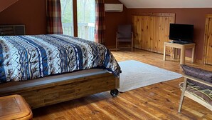 Un dormitorio con una cama, una silla, un televisor sobre un mueble y suelo de madera.
