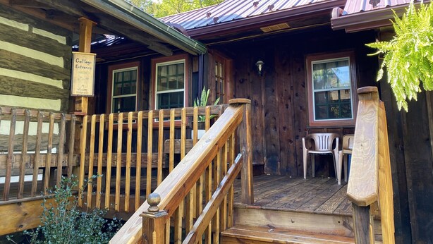 Una cabaña de madera con un porche, una escalera y un letrero que dice "Cottage Entrance".