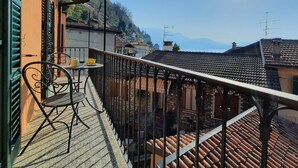 Un balcon avec une table et des chaises, donnant sur une ville aux toits de tuiles et surmontée d’une montagne.