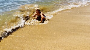 Une scène de plage avec un enfant qui joue dans l’eau, un ciel dégagé et des montagnes à l’horizon.