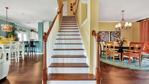 Eine Treppe mit Holzboden und weißen Geländern führt zu einem Essbereich mit einem Kronleuchter.