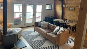 Ein gemütliches Wohnzimmer mit Ledersofa, Couchtisch und Kamin. Es gibt einen Essbereich mit Tisch und Stühlen sowie einen Blick ins Freie durch große Schiebegläser.