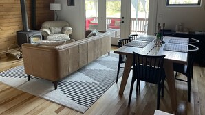 Ein gemütliches Wohnzimmer mit einer Couch, einem Esstisch mit Stühlen, einem Kamin und Blick ins Freie durch eine Schiebetür.