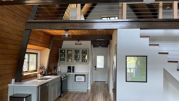 Eine moderne Loft-Küche mit Holzbalken, einem Essbereich mit brauner Ledersofa und einer Treppe, die zu einer oberen Ebene führt.