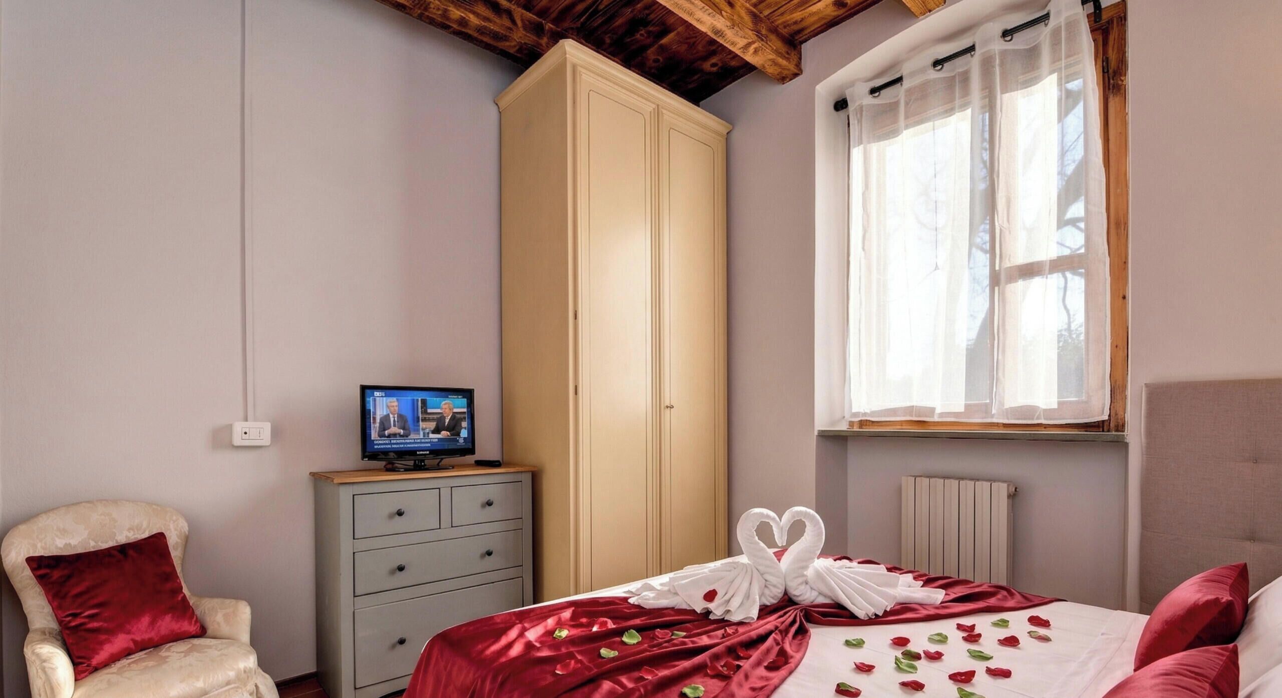 Ein Schlafzimmer mit einem Bett, einem Kleiderschrank, einem Fernseher, einem Sessel und einem Fenster mit Vorhängen.