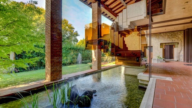 Un edificio moderno con fachada de ladrillo, un patio con paredes de vidrio y una pequeña fuente de agua.