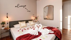 Una cama cuidadosamente hecha con sábanas blancas, un edredón rojo y dos toallas con forma de cisne. Hay una pared con un espejo y una decoración que dice 'bésame buenas noches'.