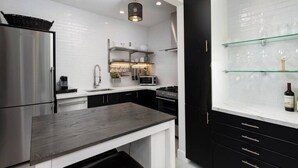 A modern kitchen with a stainless steel refrigerator, a microwave, and a gas stove. There is a black countertop and white cabinets. - Luxury Beach Studio — 2 blocks to the Beach and Funk Zone (Santa Barbara)