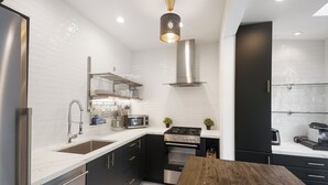 A modern kitchen with white subway tiles, stainless steel appliances, and a wooden dining table. - Luxury Beach Studio — 2 blocks to the Beach and Funk Zone (Santa Barbara)