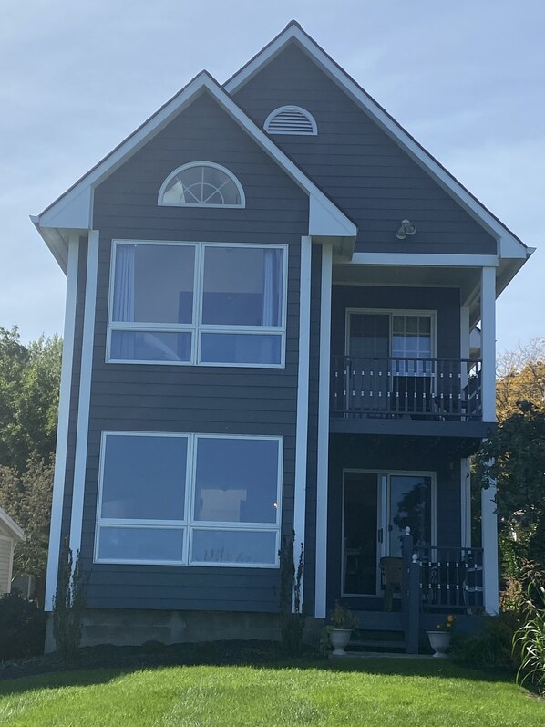Une maison à deux étages avec un balcon au deuxième étage, de grandes fenêtres et une porte d’entrée.